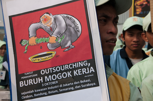 資本主義者が派遣労働者から利益をしぼり取る様子が描かれた風刺画。「アウトソーシングを止めろ」と書かれている３日、西ジャワ州ブカシ県の東ジャカルタ工業団地